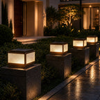 Four post cap lights on dark stone piers beside a lit modern house