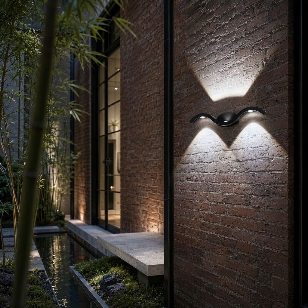 Two wave wall lights on dark brick beside glass doors and bamboo planting