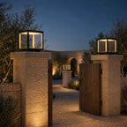 Pair of cube pillar lights on rustic stone gate posts beside a wooden garden gate at dusk