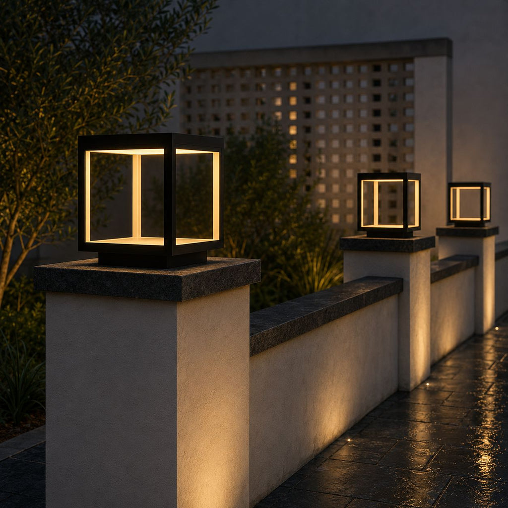 Black stainless steel cube pillar light on a white garden wall, with two more lights along the wall at dusk