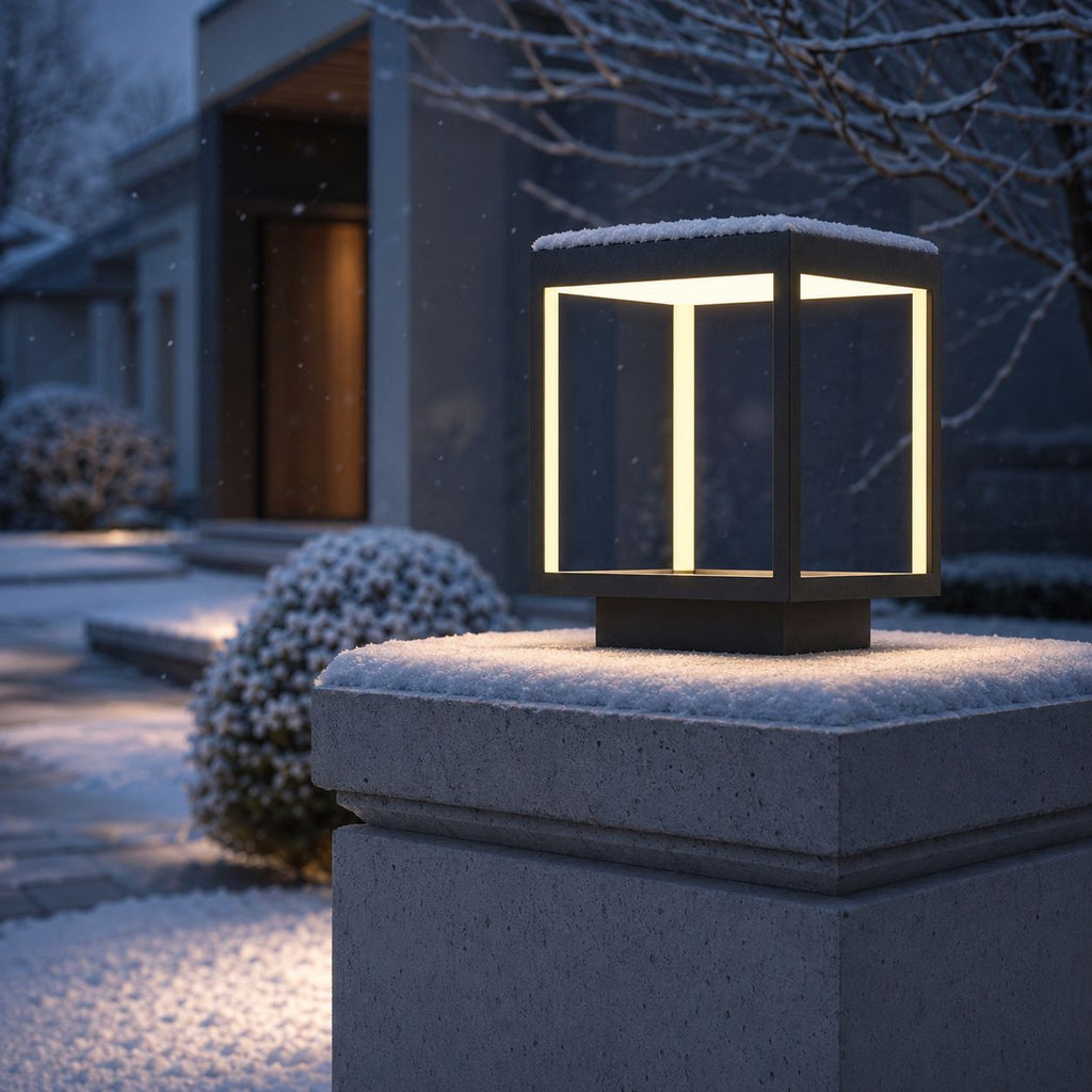 Outdoor pillar light lit in winter with snow resting on its top panel