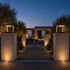 Two large cube pillar lights on stone gate piers at a modern driveway entrance at dusk
