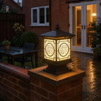 Tall lantern post cap on a brick pier beside a lit patio and French doors