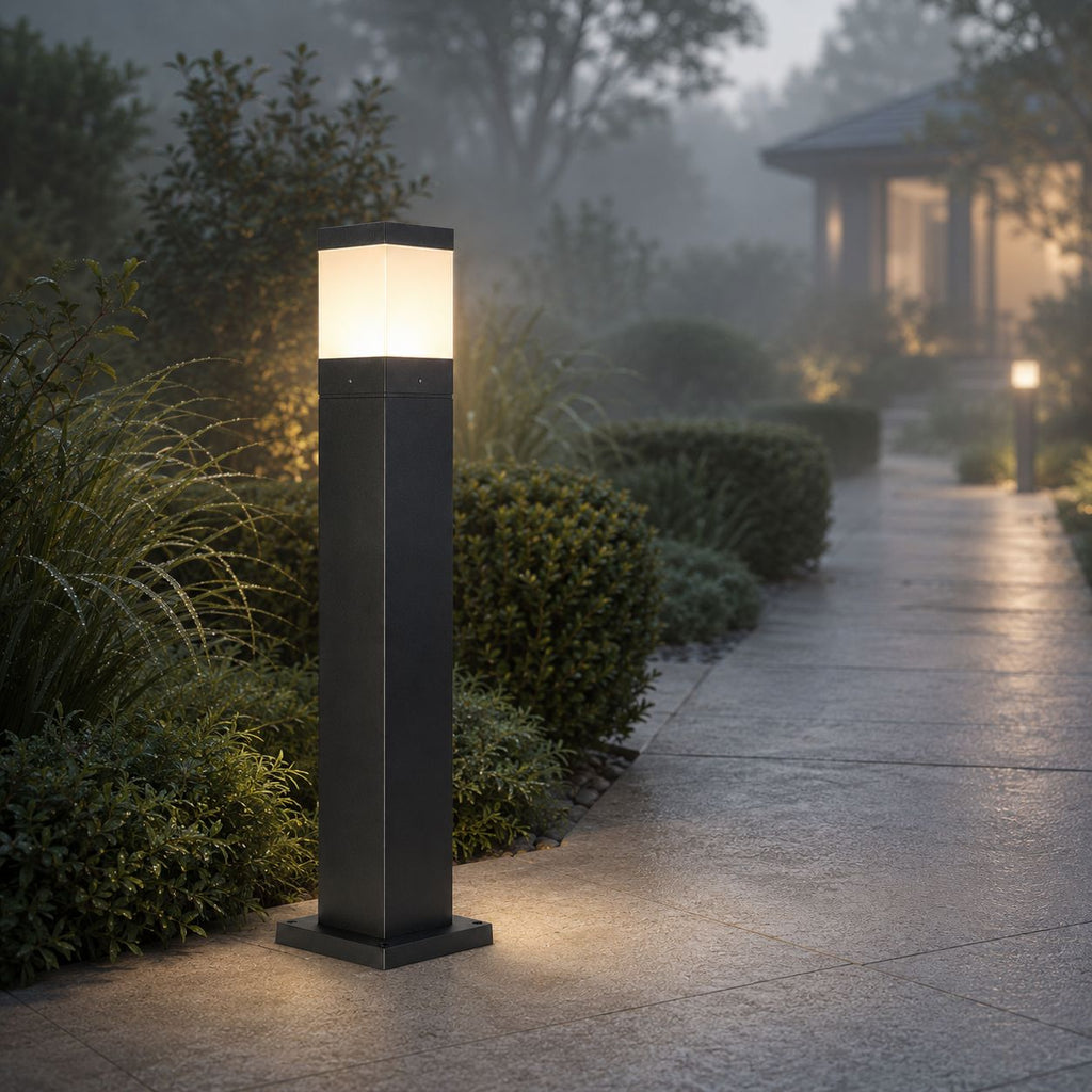 Bollard light glowing through morning mist beside a clipped hedge