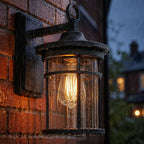 Caged glass wall lantern lit on wet red brick in the rain