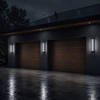 Two louvre wall lights flanking a garage door on a wet driveway at dusk