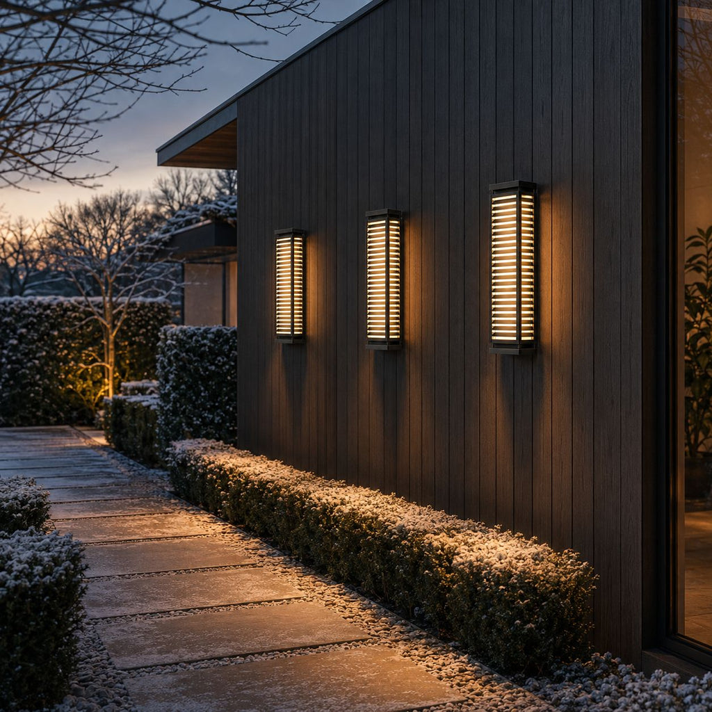 Three louvre wall lights spaced along a dark timber facade above hedging