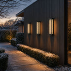 Three louvre wall lights spaced along a dark timber facade above hedging