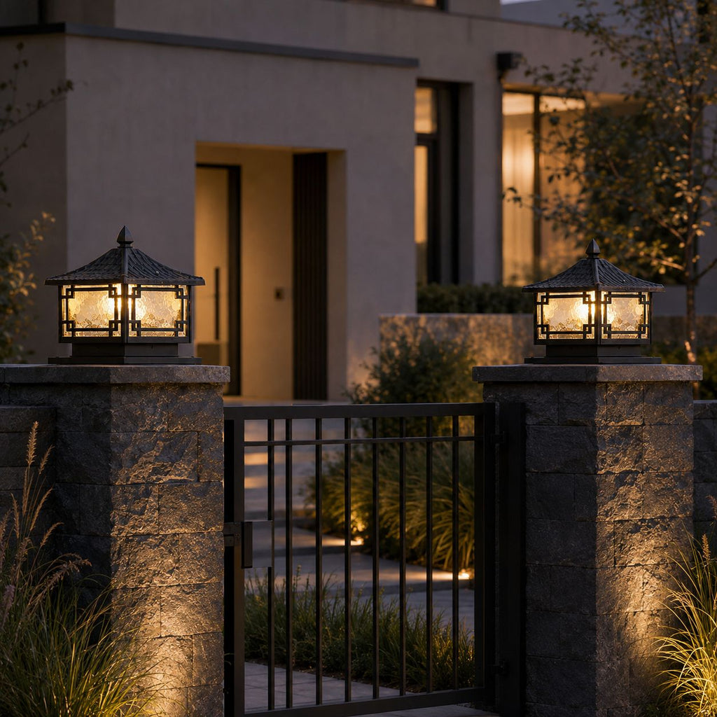 Pair of traditional pillar lanterns on stone gate posts flanking an iron gate at dusk