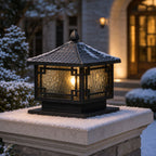 Pillar lantern with snow settled on its roof beside snow-covered shrubs