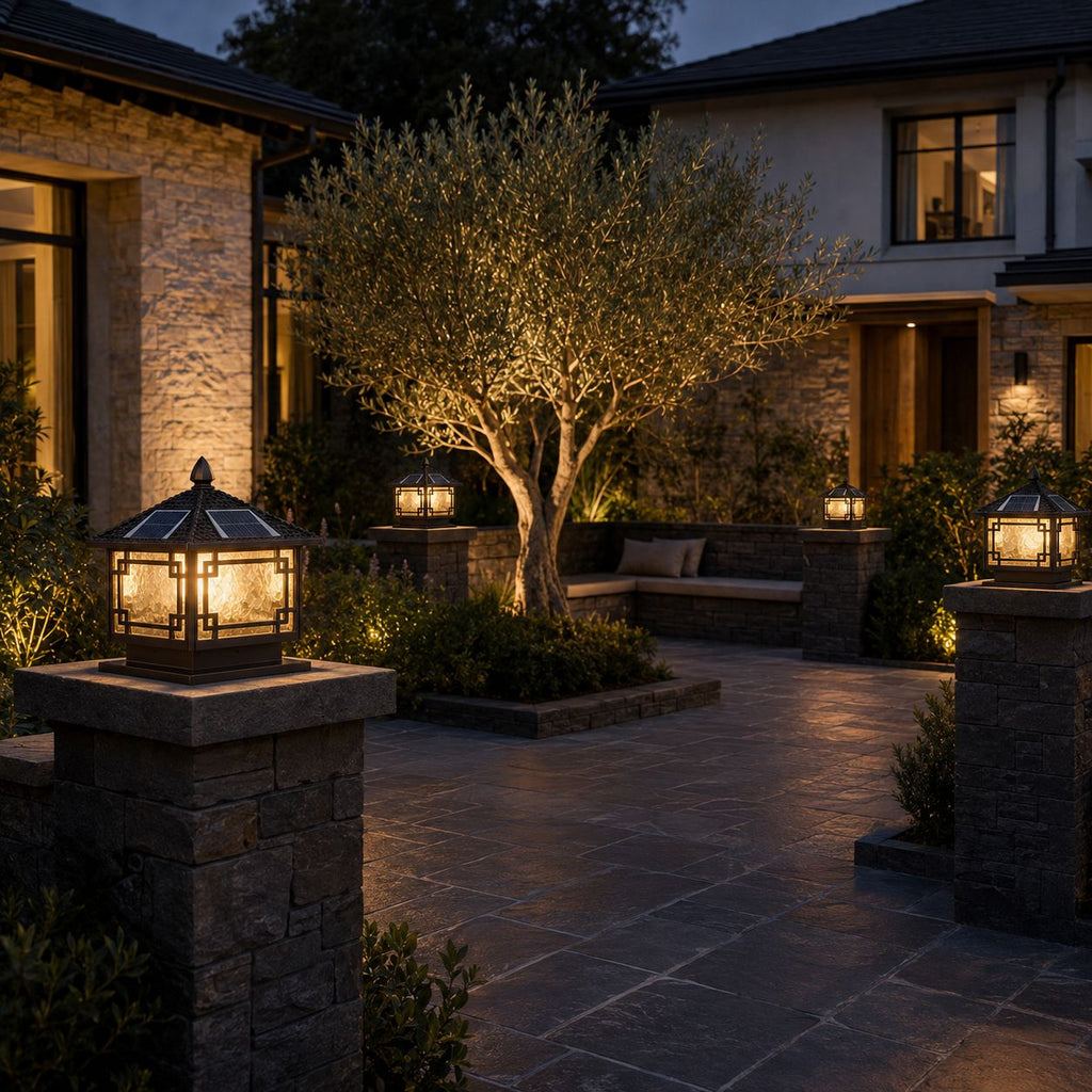 Two pillar lanterns on stone piers outside a stone house with an olive tree at dusk
