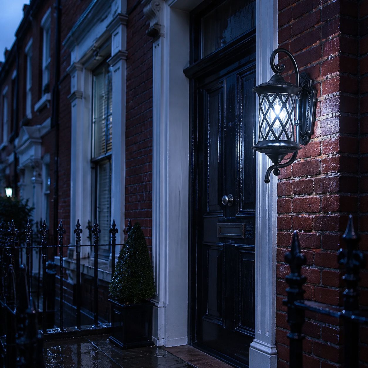 Lattice wall lantern lit on a wet street beside black railings at night