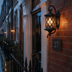 Lattice wall lantern on brick beside a house number plaque on a wet street