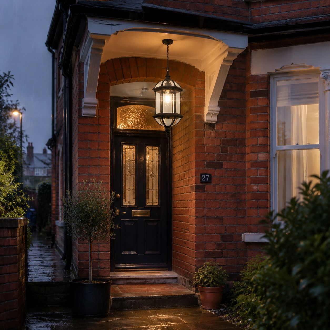 Domed pendant lantern lit in a brick porch above a dark front door at night