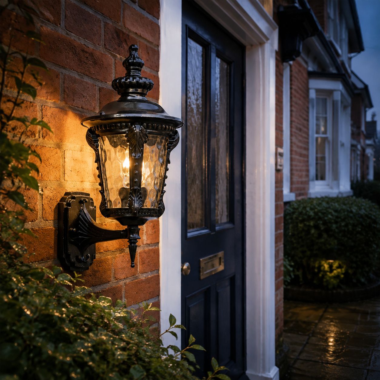 Black hammered glass wall lantern lit beside a dark front door on red brick