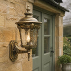 Bronze hammered glass wall lantern on stone beside a green window in the rain