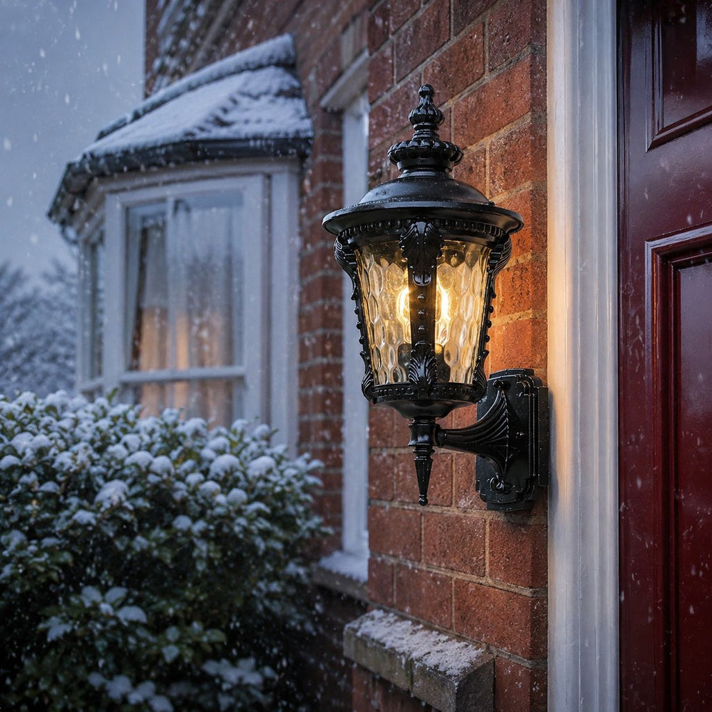 Black hammered glass wall lantern beside a red front door during snowfall