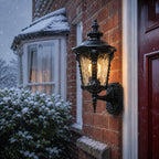 Black hammered glass wall lantern beside a red front door during snowfall