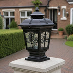 Black scrollwork pillar light on a pale stone pier beside a brick driveway