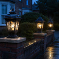 Three scrollwork pillar lights lit along a low brick wall on a wet street