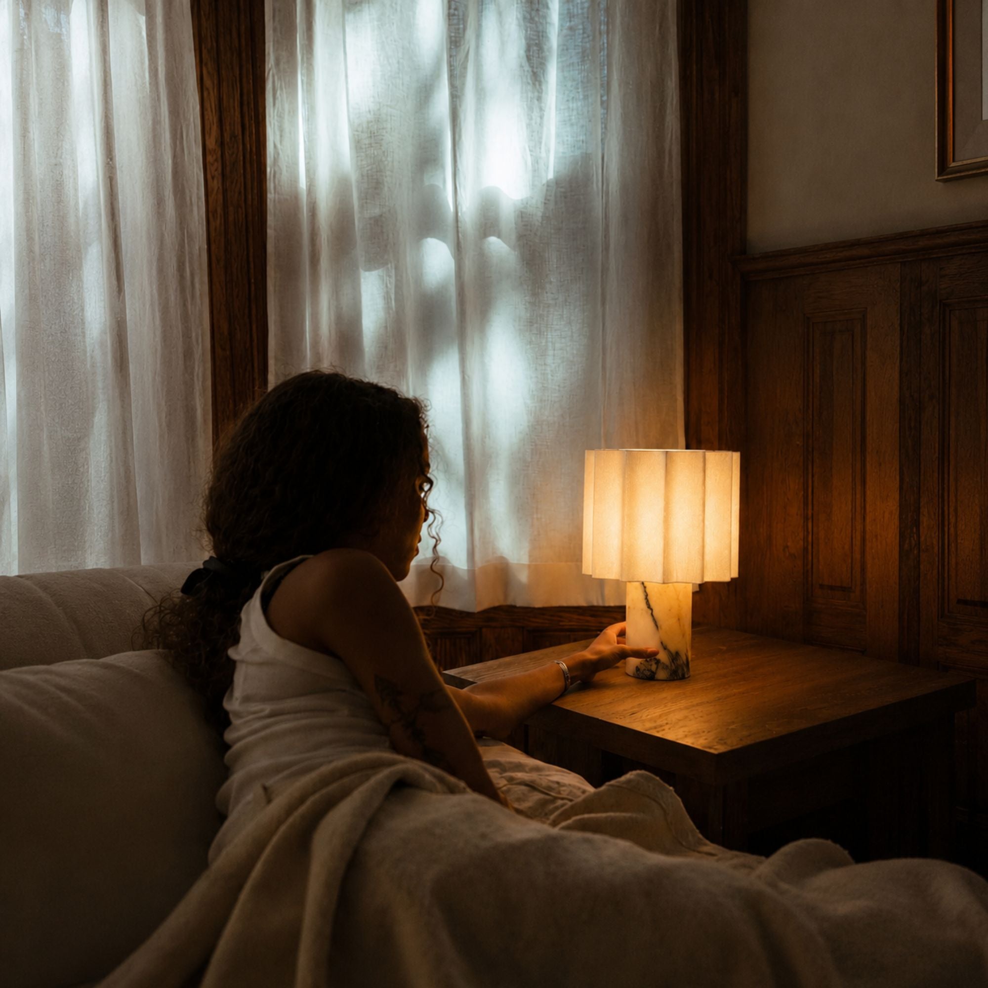 Woman relaxing beside a glowing marble table lamp in a cozy bedroom with warm ambient lighting