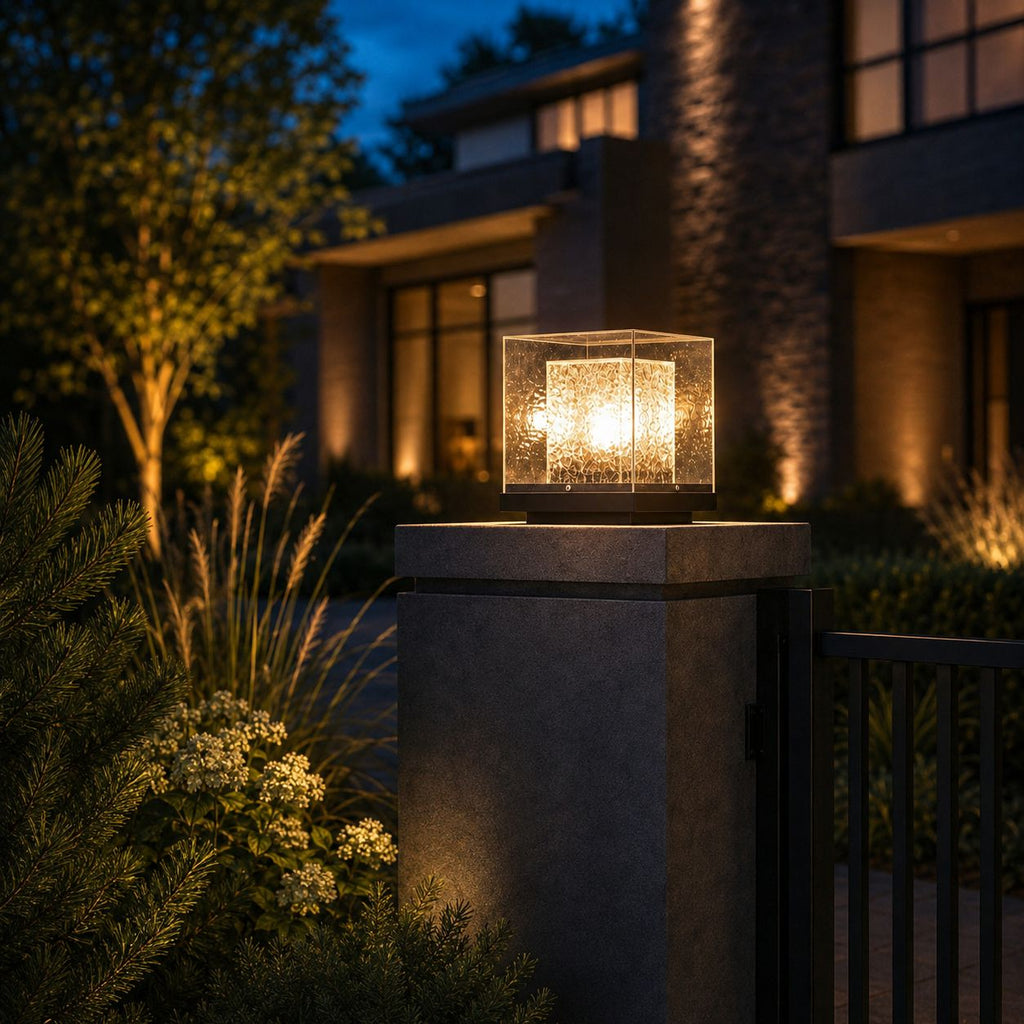 Post cap light glowing on a concrete gate pier beside ornamental grasses