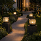 Four post cap lights on dark stone piers lining a garden path at dusk