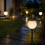 Solar globe path lights beside a lawn and stepping stones on wet paving