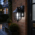 Nautical caged sconce on brick beside a doorway with potted topiary