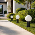 Three globe bollard lights along a lawn edge beside a white rendered house