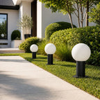Three globe bollard lights along a lawn edge beside a white rendered house