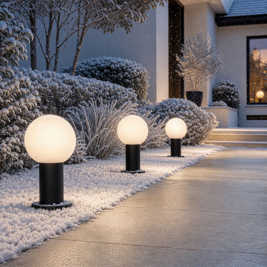 Globe bollard lights along a snow-covered garden path in winter