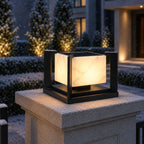 Marble pillar light lit in snow beside frosted topiary at a house entrance