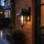 Black nautical caged sconce lit beside a brick house entrance at dusk