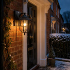 Nautical caged sconce lit beside a doorway with snow on the planting