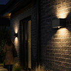 Two up and down wall lights along a dark brick wall lighting a path