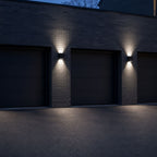 Three up and down wall lights spaced along a dark garage facade