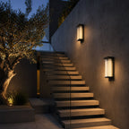 Two tall reeded wall lights on a dark facade beside steps and an olive tree