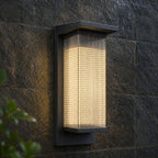 Tall reeded wall light lit in heavy rain against dark stone