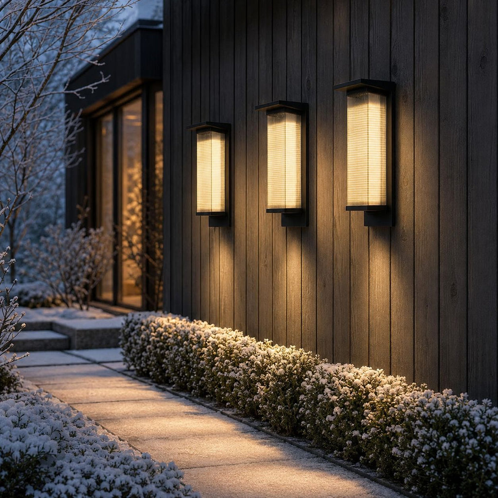 Three tall wall lights on dark timber cladding above snowy white planting