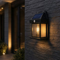 Solar motion sensor wall lantern on dark stone beside glass doors, solar panel visible