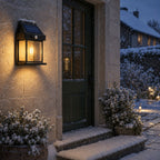 Solar motion sensor lantern with snow on its panel beside a cottage doorway