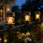Three solar lanterns clamped to a black railing above flowering planting