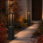 Two black LED garden bollard lights along a paved path with autumn planting at dusk