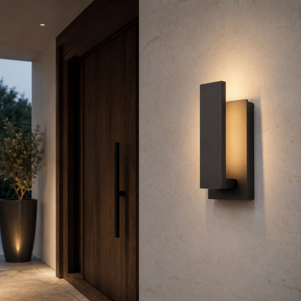 Slim black outdoor wall light on pale stone beside a dark timber front door and olive planter