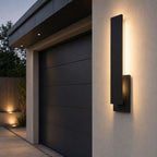 Large slim wall light beside a dark garage door on a white rendered driveway wall
