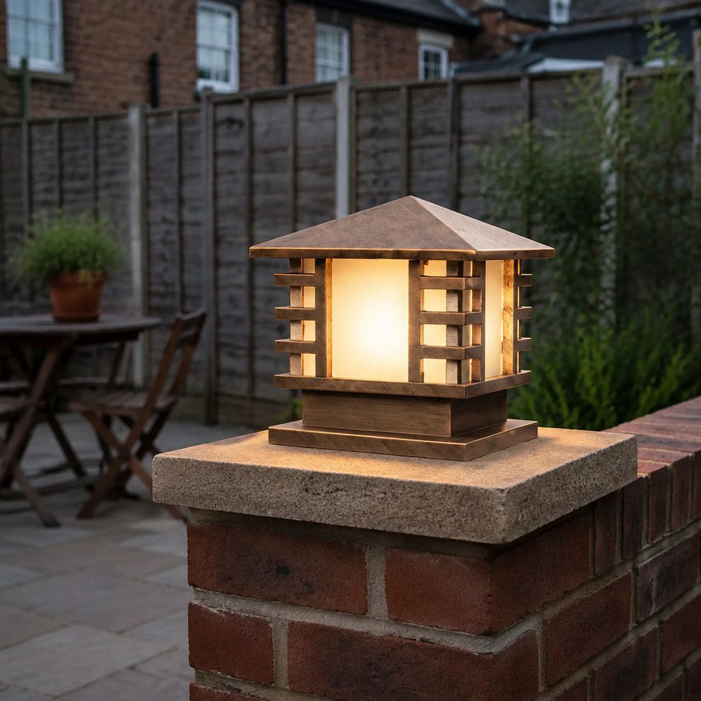 Bronze slatted post cap light lit on a brick pier beside a garden table