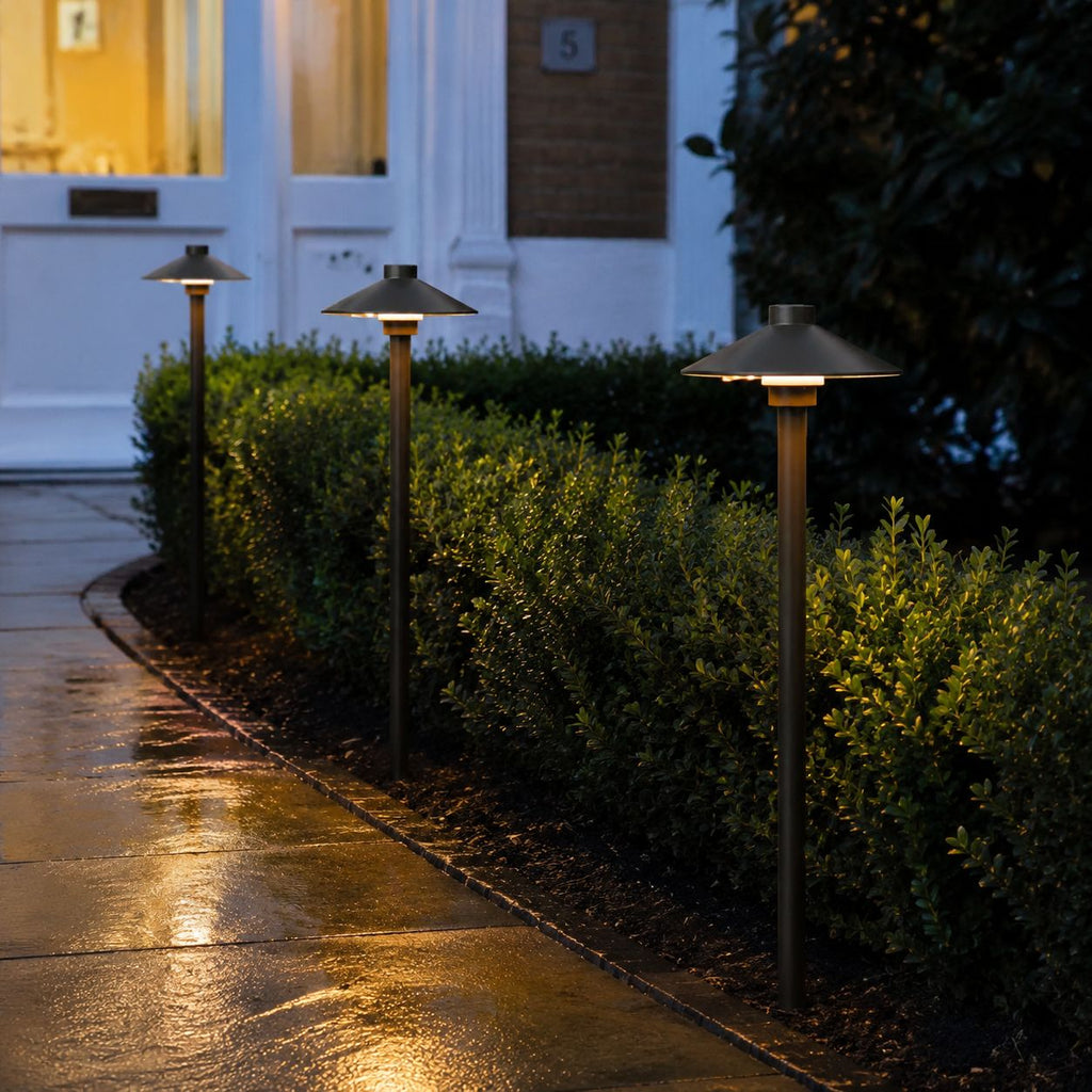Row of umbrella path lights along a wet path with clipped box hedging