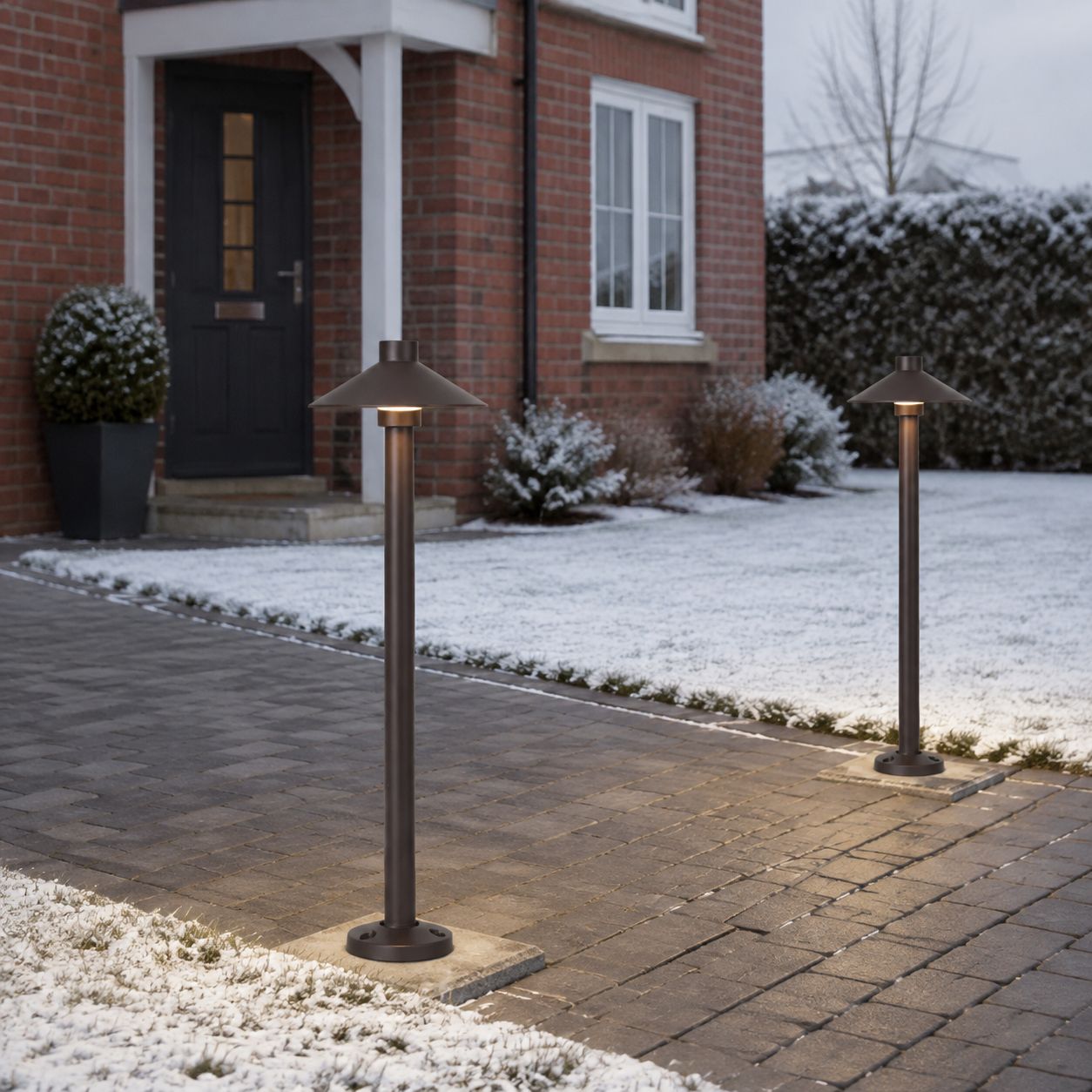 Two umbrella path lights on a snowy driveway beside a front door