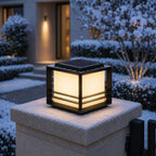 Solar pillar light on a snow-covered pillar cap beside frosted shrubs